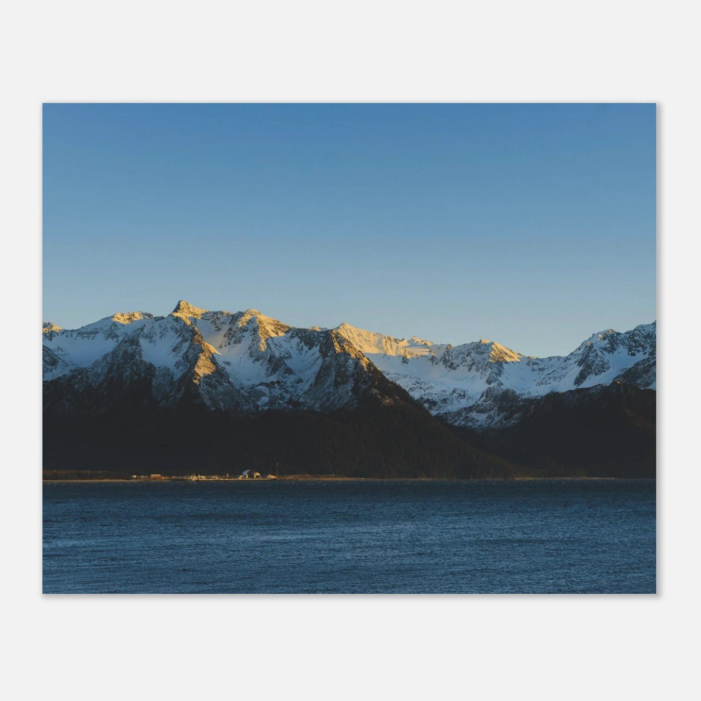 Snow-capped mountains reflected in a body of water under a clear blue sky.