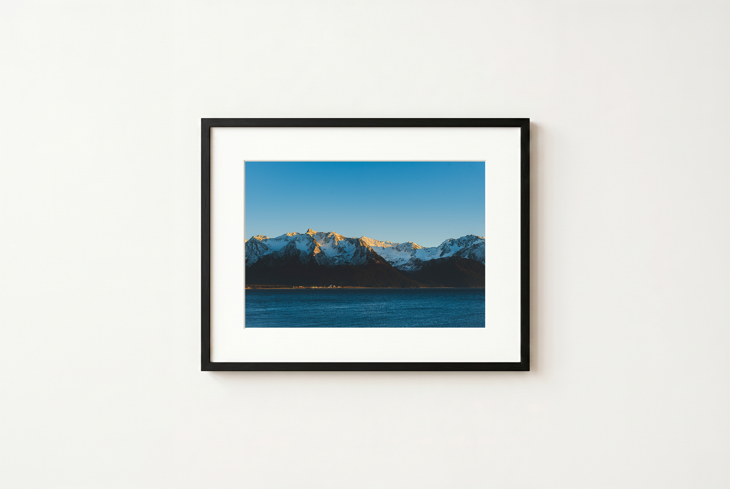 Framed photograph of a mountain landscape with a blue sky on a white wall.