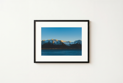 Framed photograph of a mountain landscape with a blue sky on a white wall.