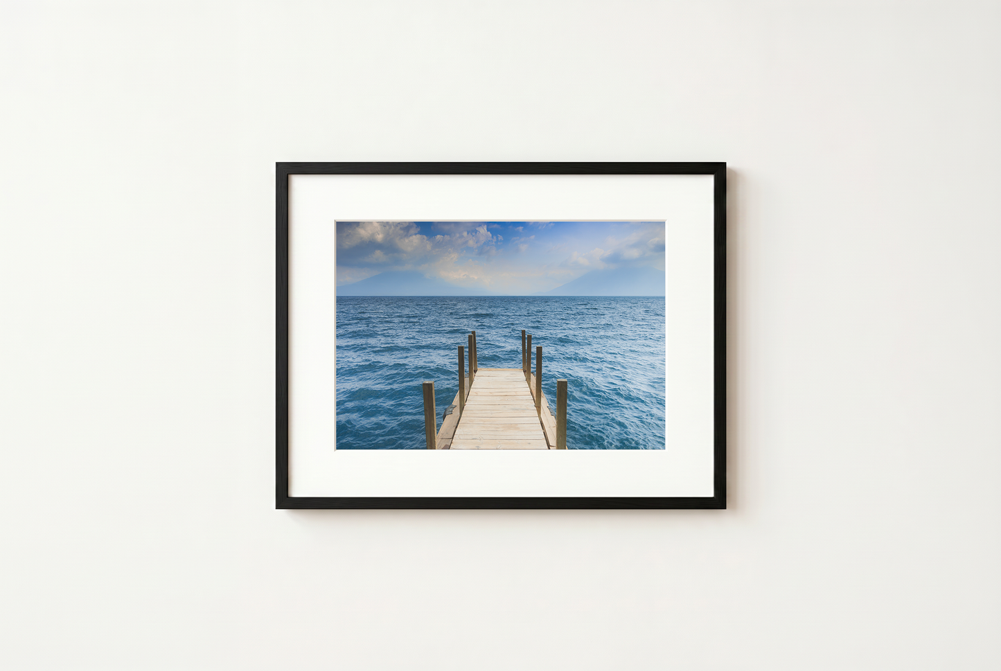 Framed photograph of a dock extending into the ocean on a white wall.