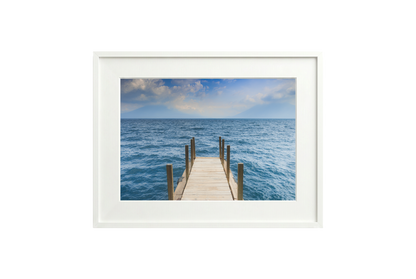 Framed artwork of a wooden dock extending into the ocean with a white frame.