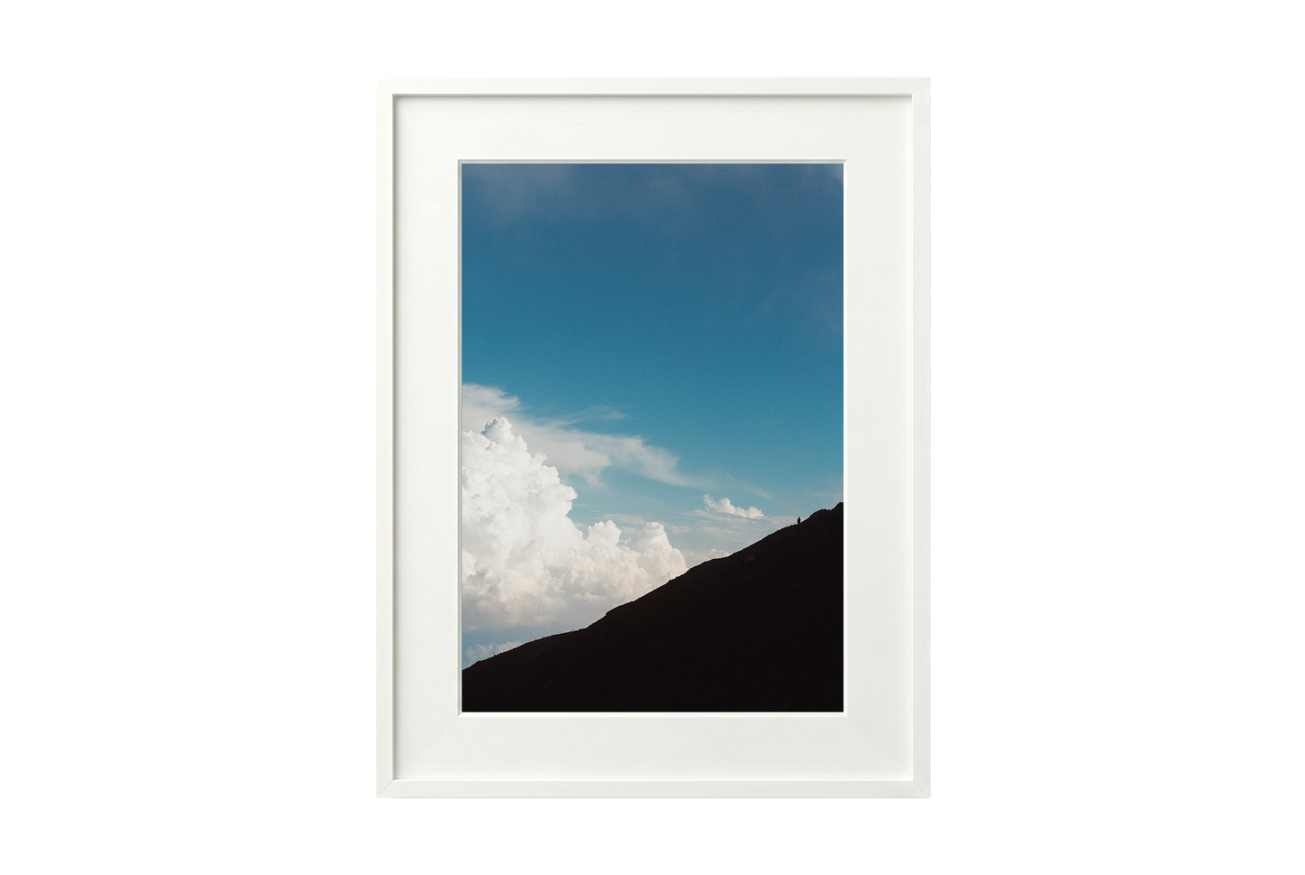 Framed photograph of a mountain landscape with a blue sky and clouds.