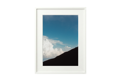 Framed photograph of a mountain landscape with a blue sky and clouds.