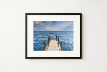 Framed photograph of a dock extending into the ocean on a white wall.