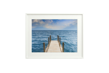Framed photograph of a dock extending into the ocean on a white wall.