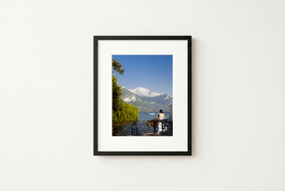Framed photograph of a scenic view with mountains and a lake on a white wall.