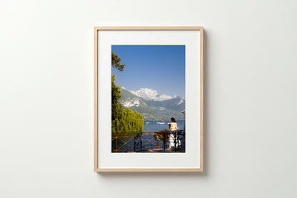 Framed photograph of a person by a lake with mountains in the background on a white wall.