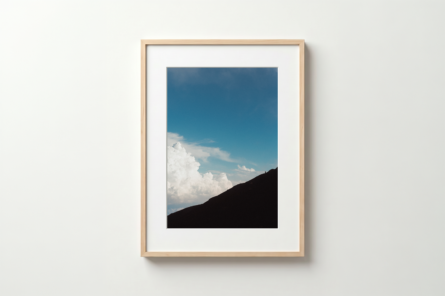 Framed photograph of a mountain and blue sky with clouds on a white wall.