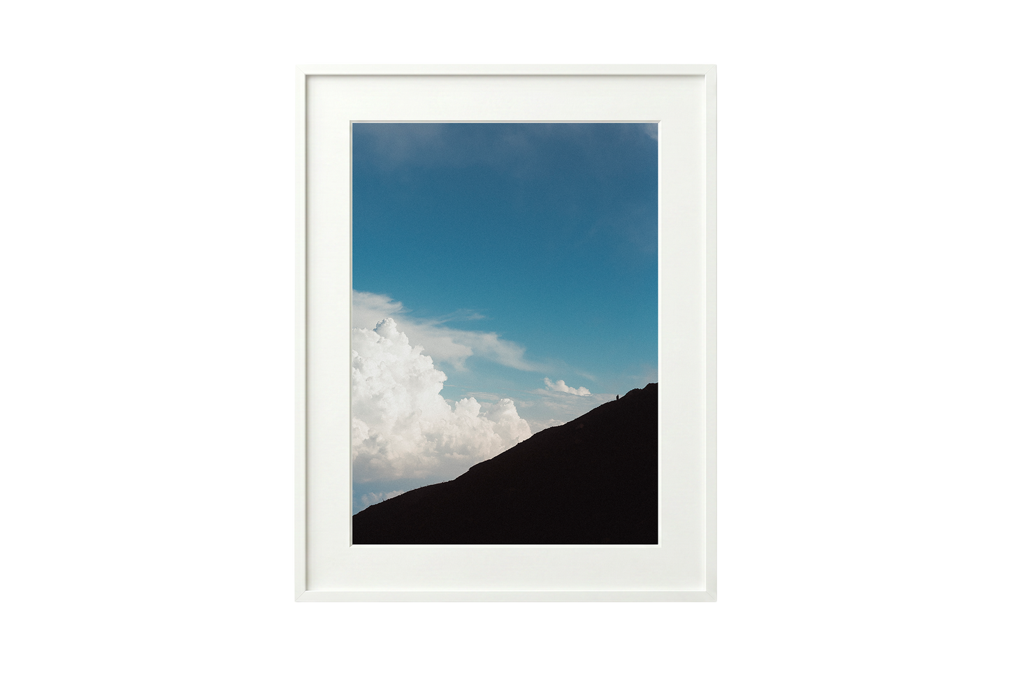 Framed photograph of a mountain landscape with a blue sky and clouds.