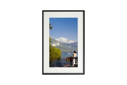 Framed artwork of a scenic view with mountains and a lake.