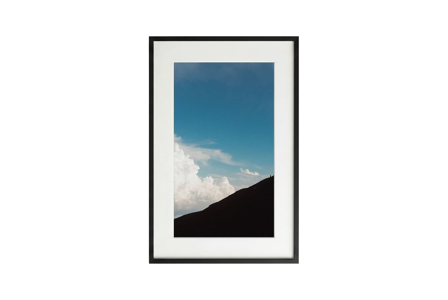 Framed picture of a mountain landscape with blue sky and clouds.