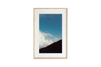Framed photograph of a mountain landscape with blue sky and clouds.