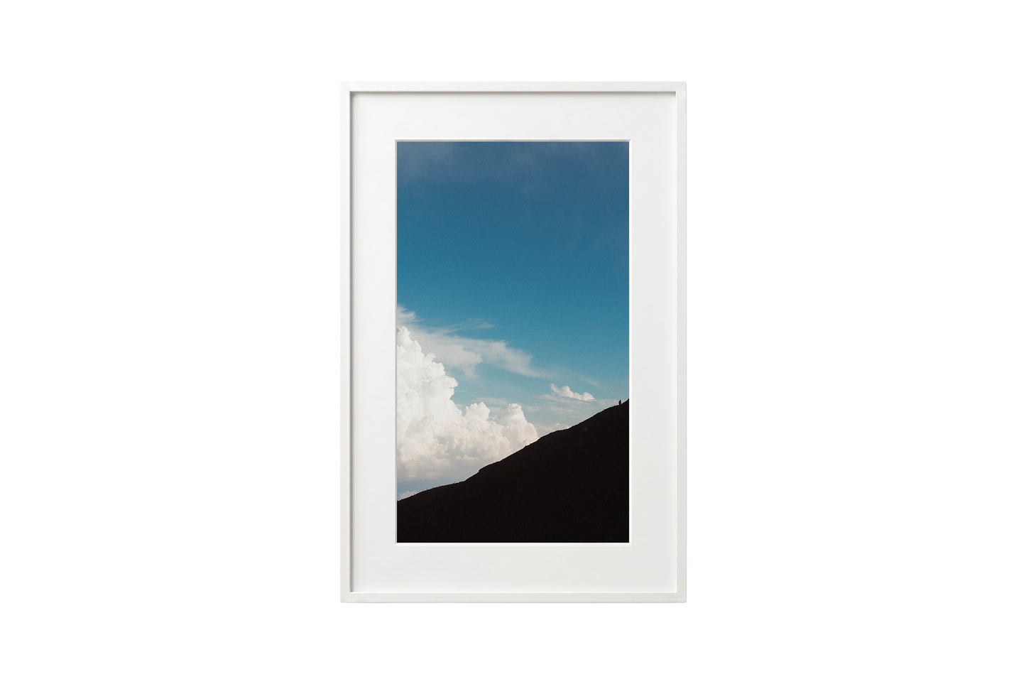 Framed photograph of a mountain landscape with blue sky and clouds.