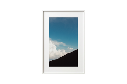Framed photograph of a mountain landscape with blue sky and clouds.