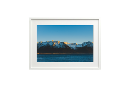 Framed photograph of a mountain range with snow and a blue sky.
