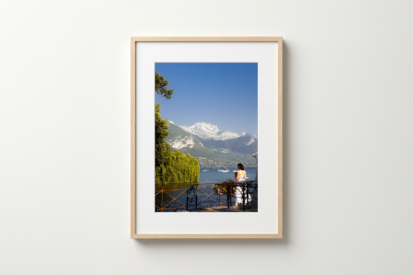 Framed photograph of a person by a lake with mountains in the background on a white wall.