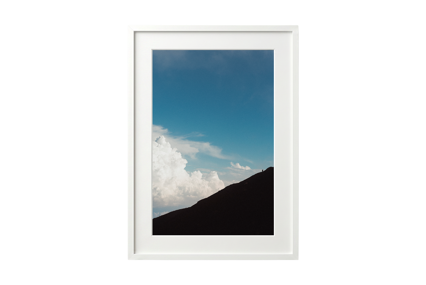 Framed picture of a mountain landscape with blue sky and clouds.