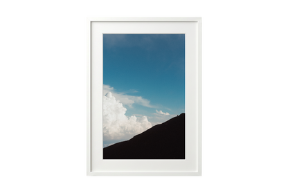Framed picture of a mountain landscape with blue sky and clouds.