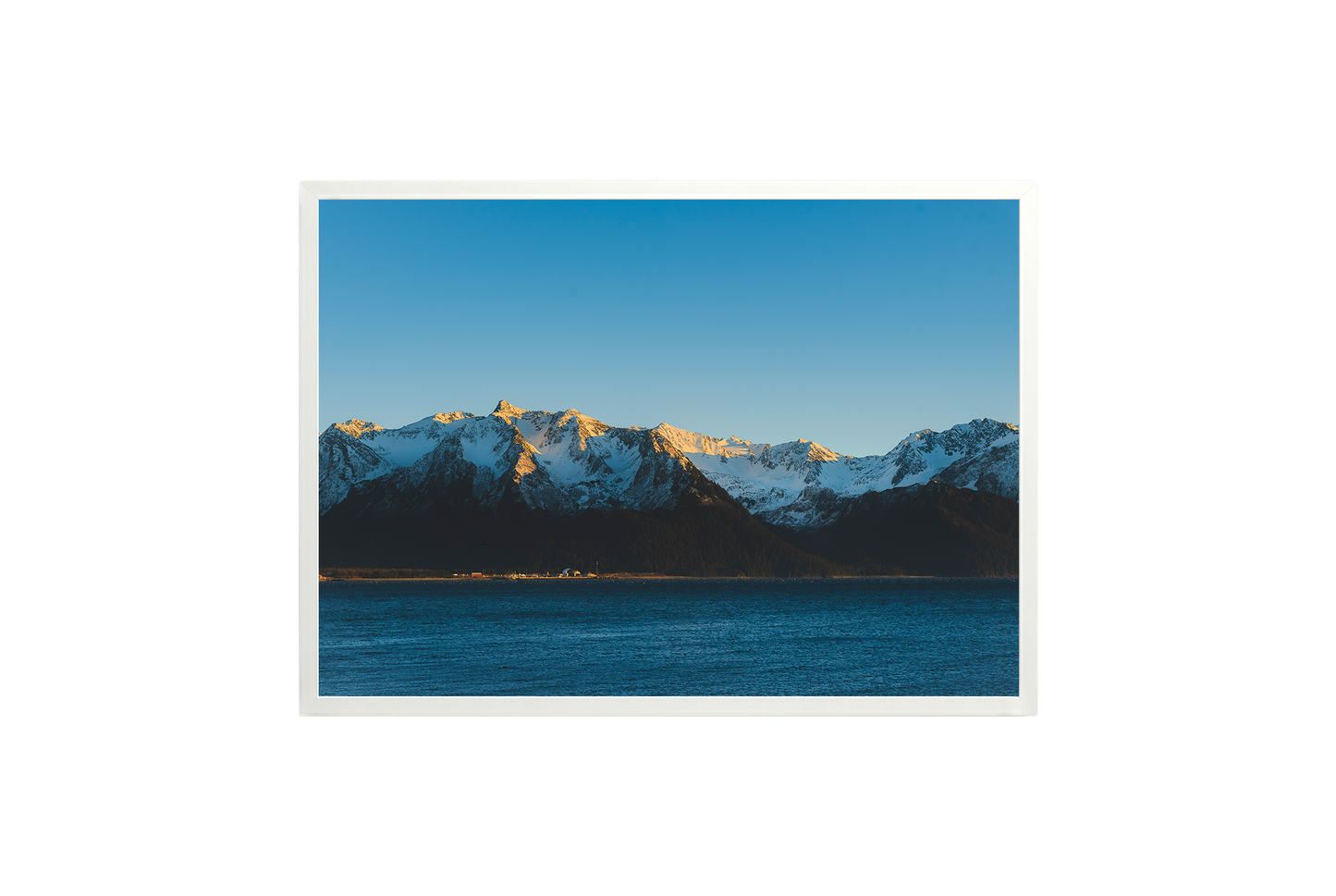 Mountain range with snow peaks over a body of water under a clear blue sky.