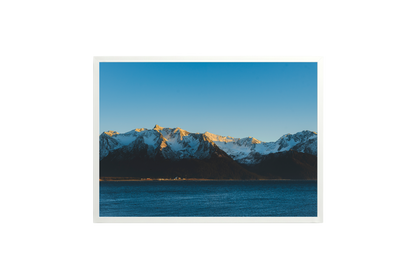 Mountain range with snow peaks over a body of water under a clear blue sky.