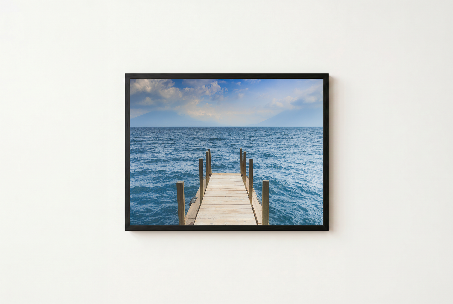 Framed photograph of a dock extending into the ocean on a white wall.