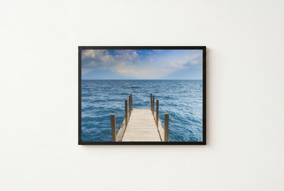 Framed photograph of a dock extending into the ocean on a white wall.
