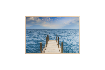 Framed photograph of a dock extending into the ocean on a white wall.