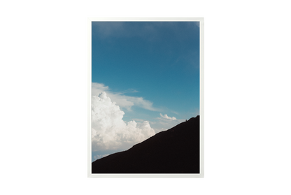 Mountain silhouette against a blue sky with clouds, framed by a white border.