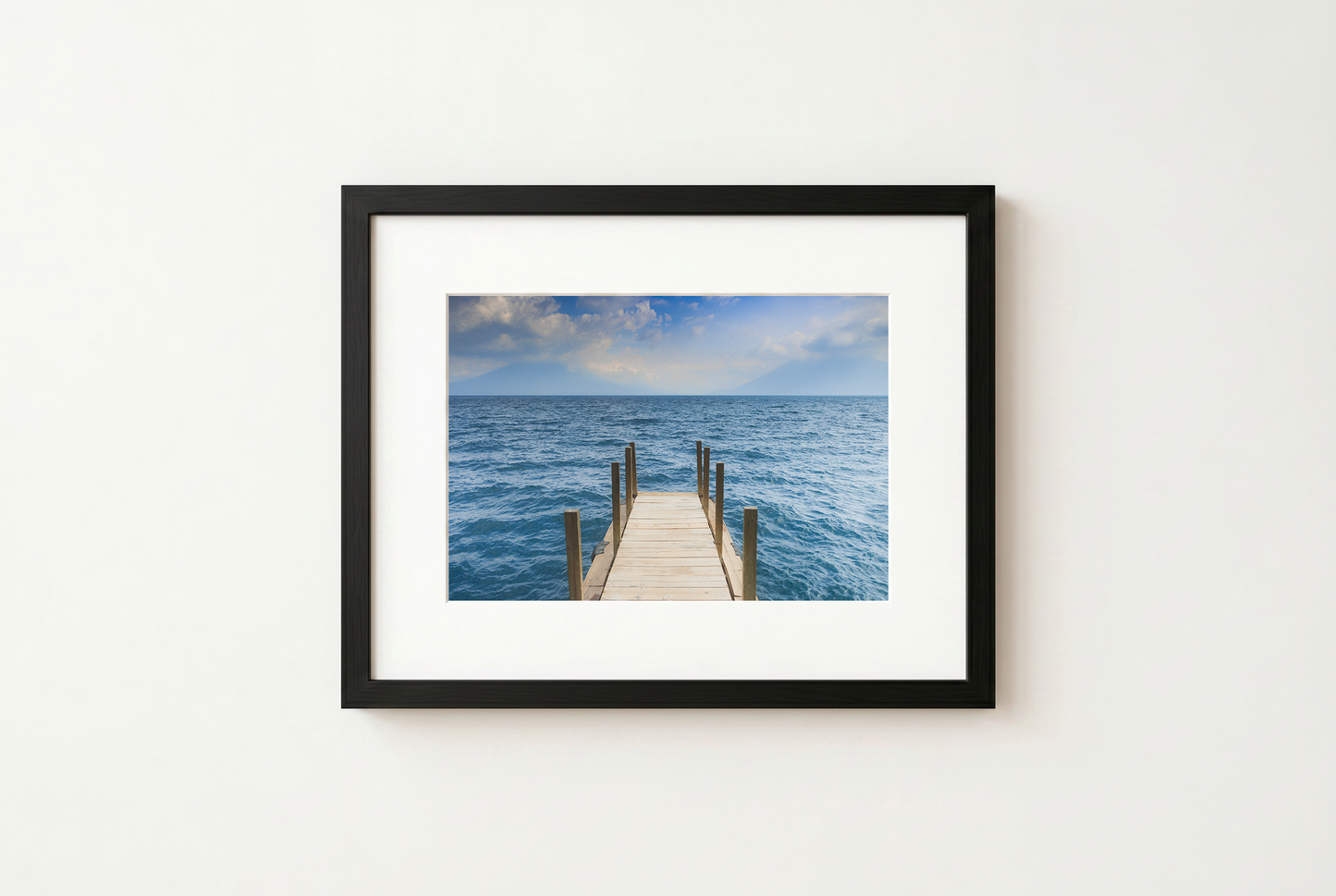 Framed photograph of a dock extending into the ocean on a white wall.