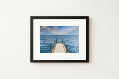 Framed photograph of a dock extending into the ocean on a white wall.