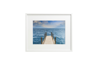 Framed picture of a wooden dock extending into the ocean with a white frame.