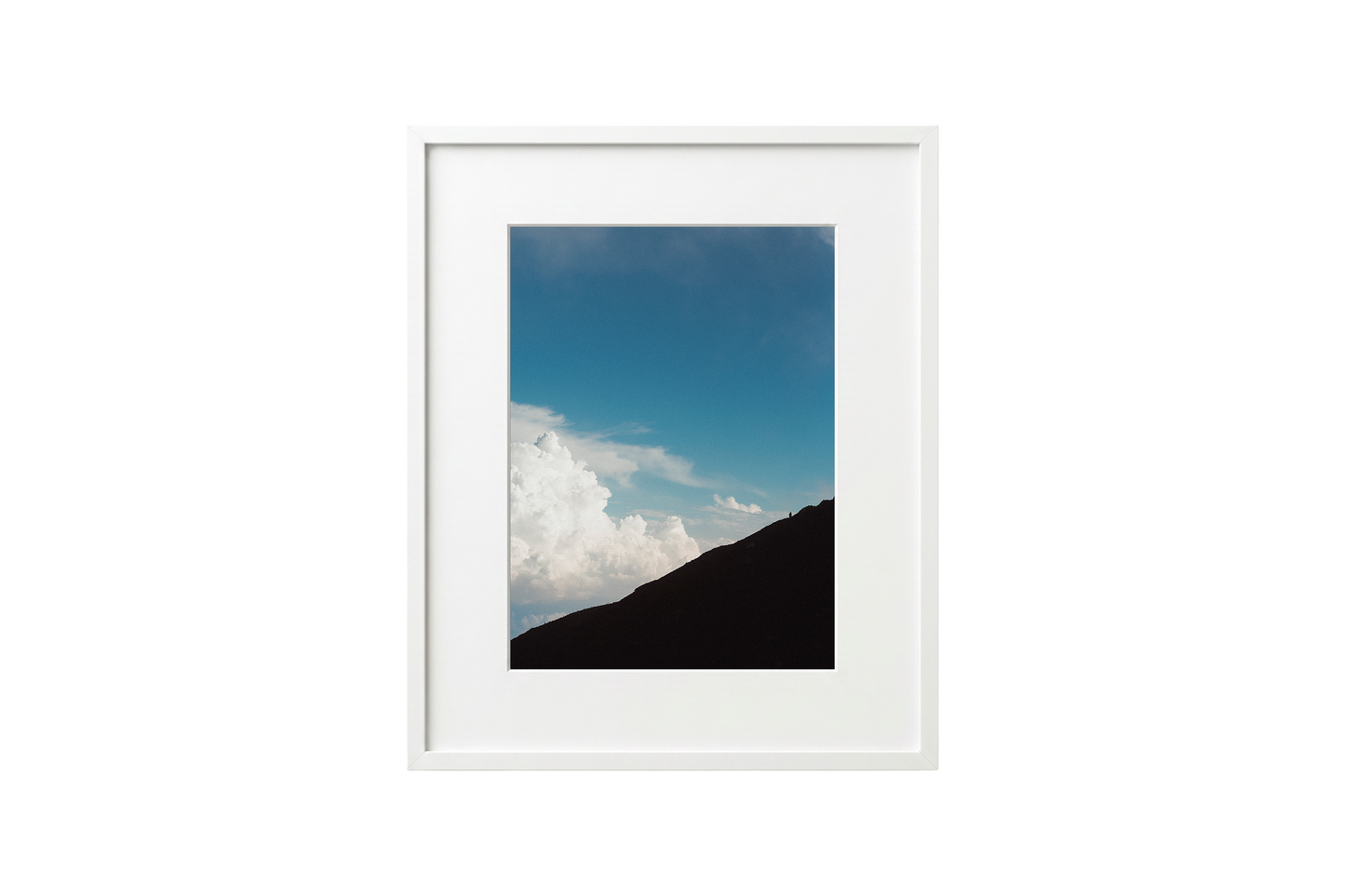 Framed photograph of a mountain landscape with blue sky and clouds.