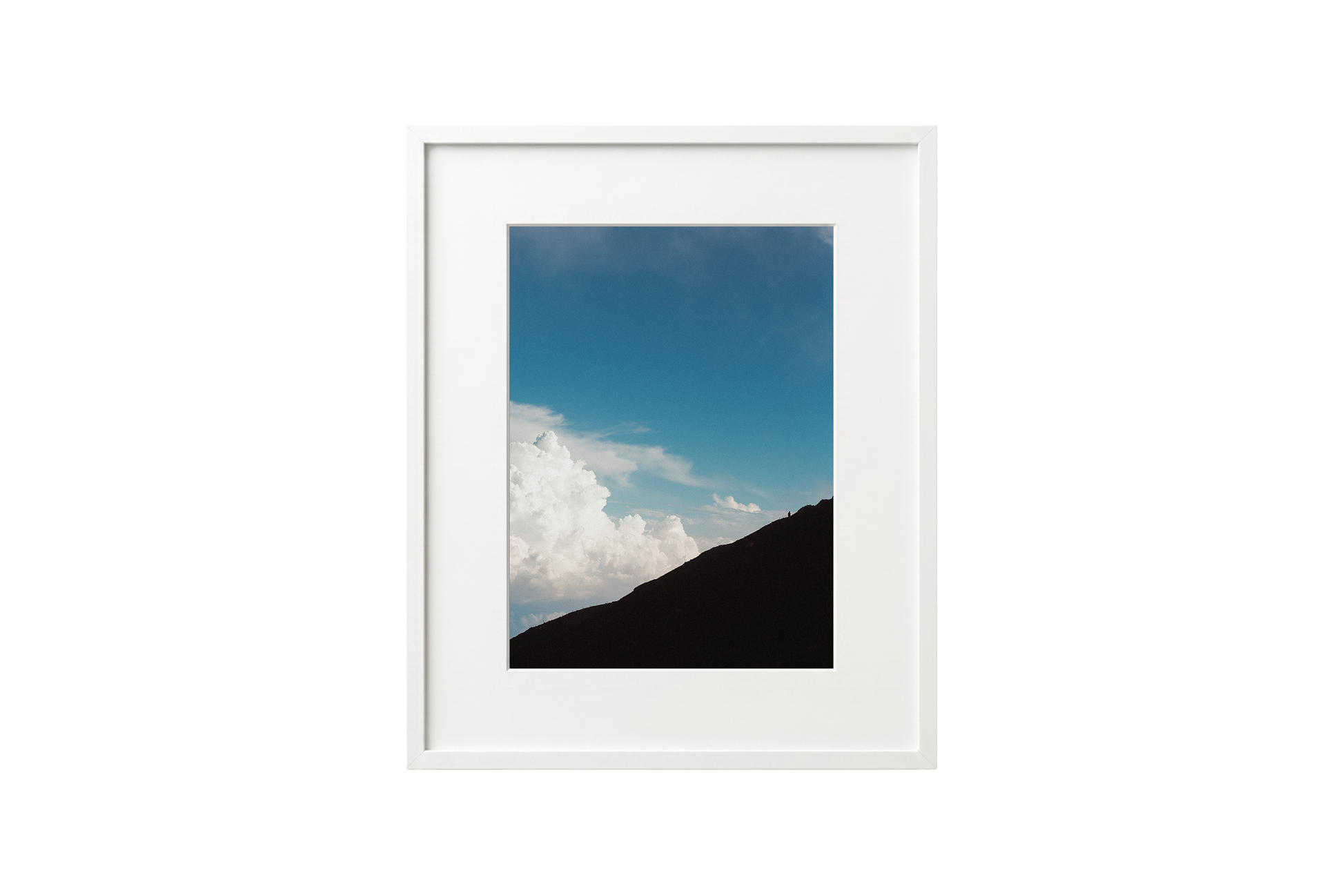 Framed photograph of a mountain landscape with blue sky and clouds.