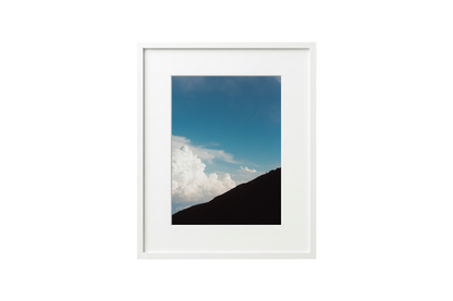 Framed photograph of a mountain landscape with blue sky and clouds.