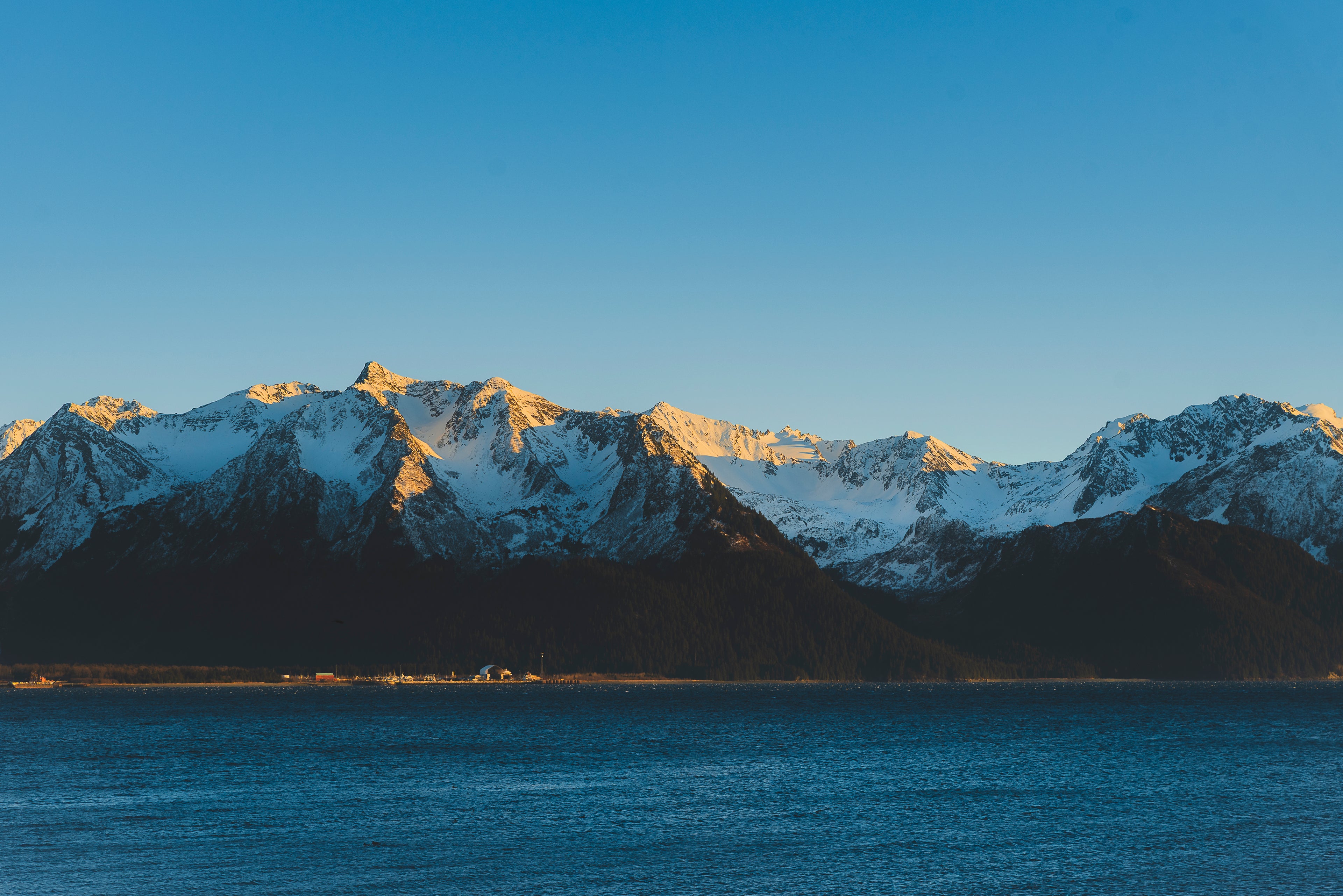 Blue toned, calming Fine Art Photograph of Snow-capped mountains with a clear blue sky and water in the foreground