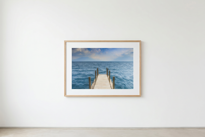 Framed photograph of a dock extending into the ocean on a white wall.