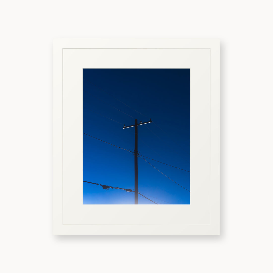
Power — 11x14, white frame. A utility pole and crossing wires against a saturated blue evening sky.