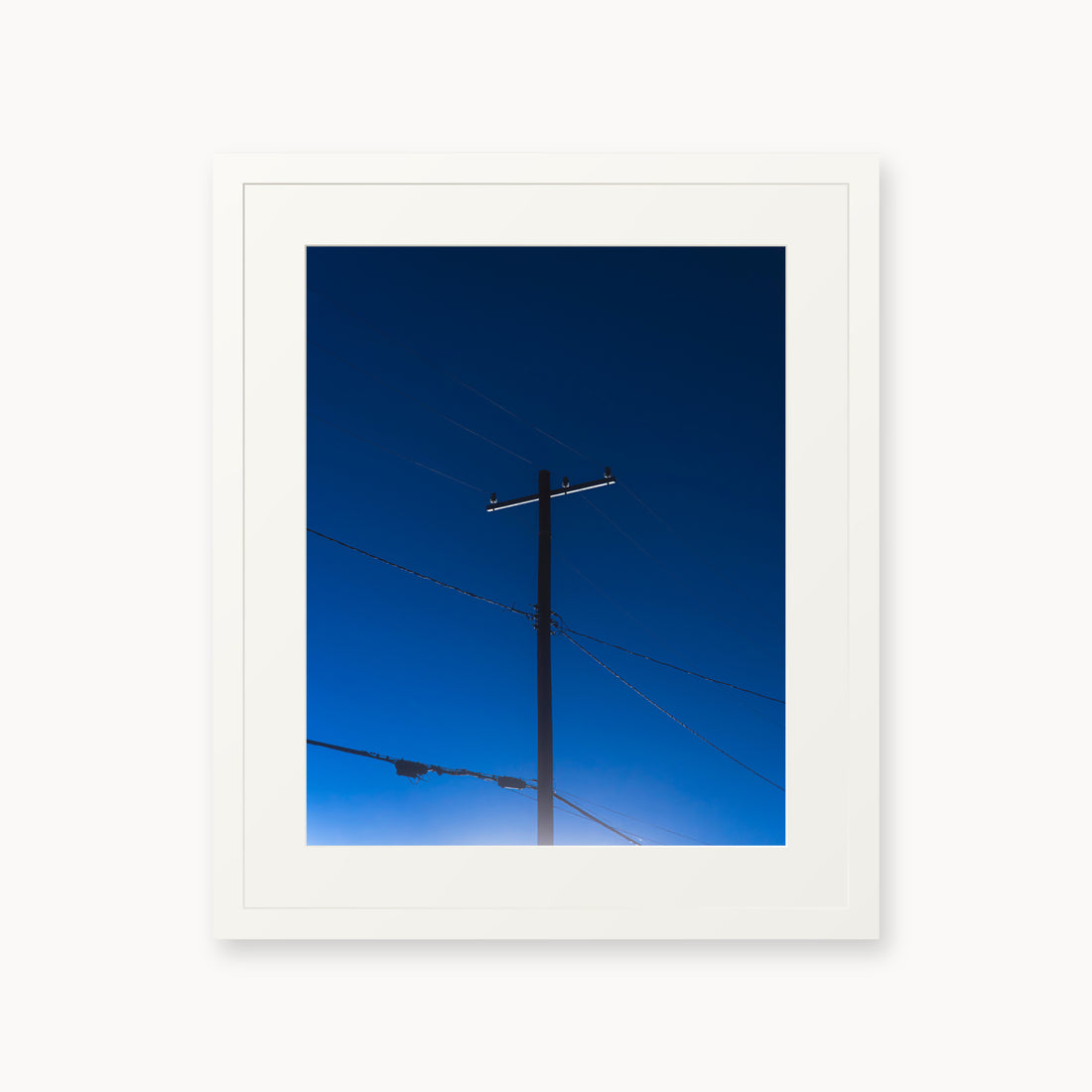 
Power — 16x20, white frame. A utility pole and crossing wires against a saturated blue evening sky.