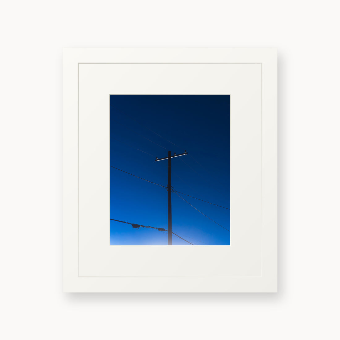 
Power — 8x10, white frame. A utility pole and crossing wires against a saturated blue evening sky.