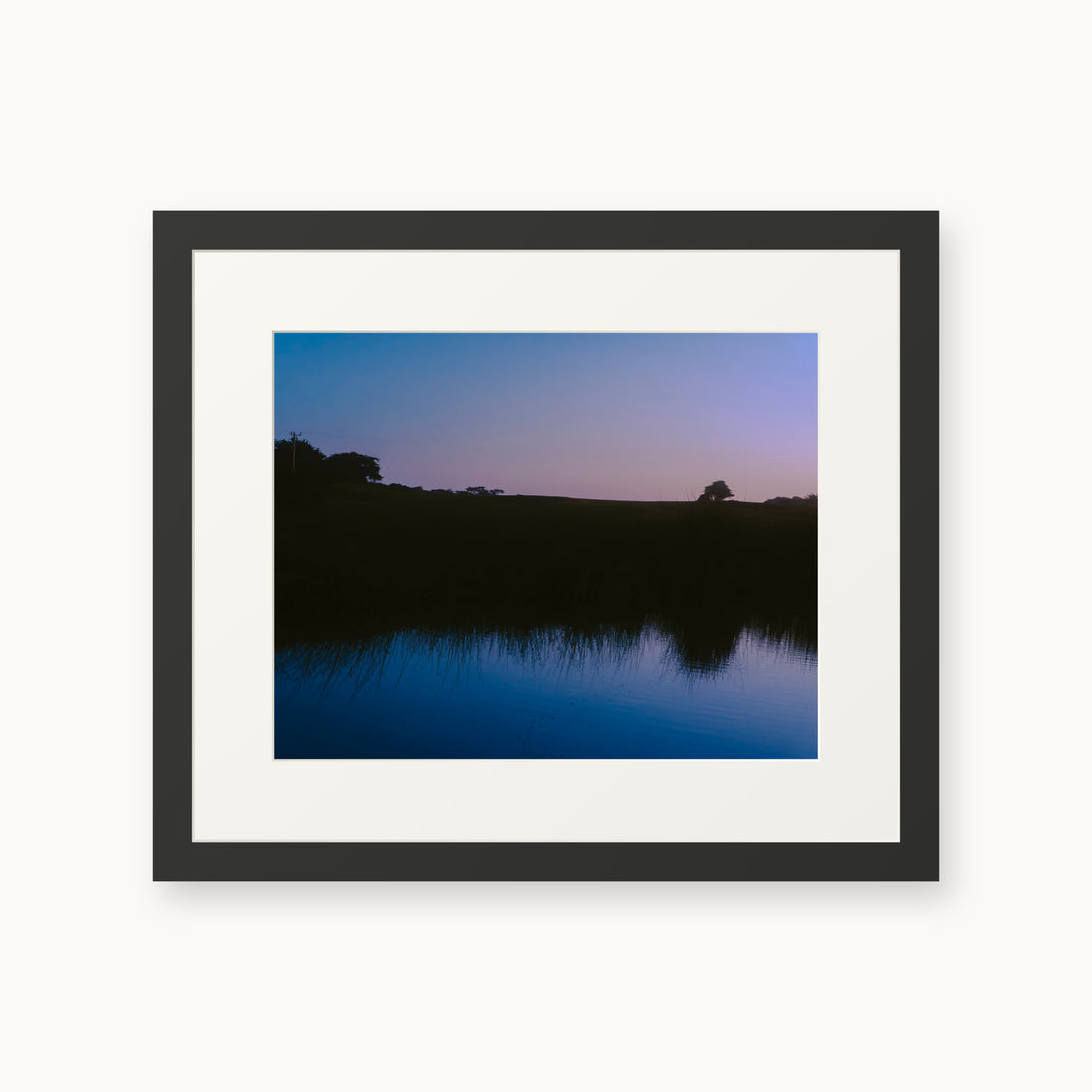 
What Lays Beneath — 11x14, black frame. Dark trees and a twilight shoreline reflected across blue water.