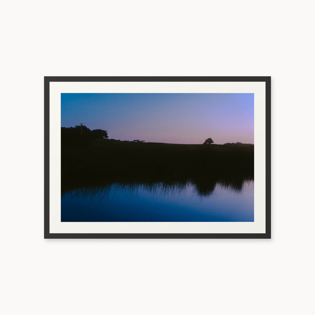 
What Lays Beneath — 24x36, black frame. Dark trees and a twilight shoreline reflected across blue water.