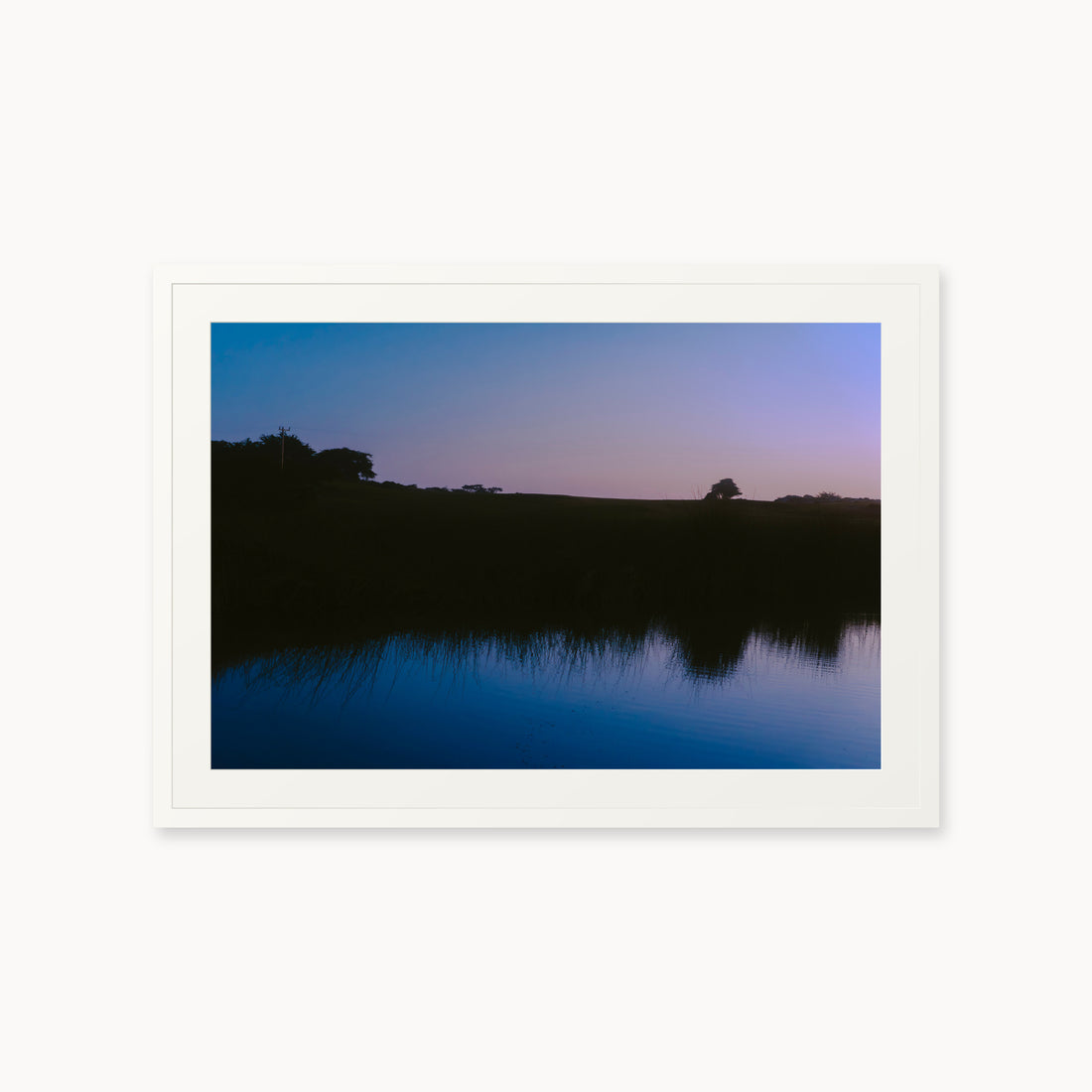 
What Lays Beneath — 24x36, white frame. Dark trees and a twilight shoreline reflected across blue water.