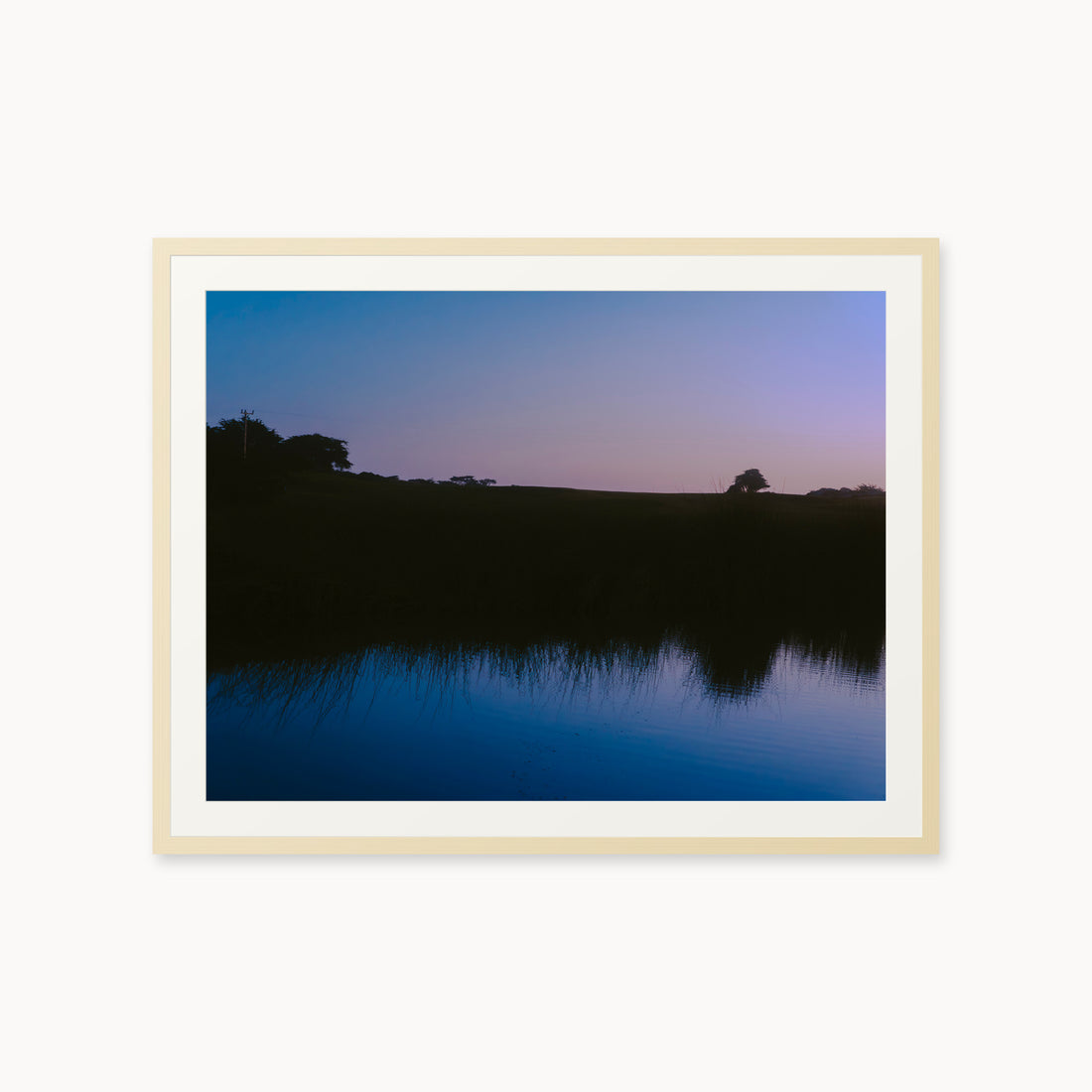 
What Lays Beneath — 30x40, maple frame. Dark trees and a twilight shoreline reflected across blue water.