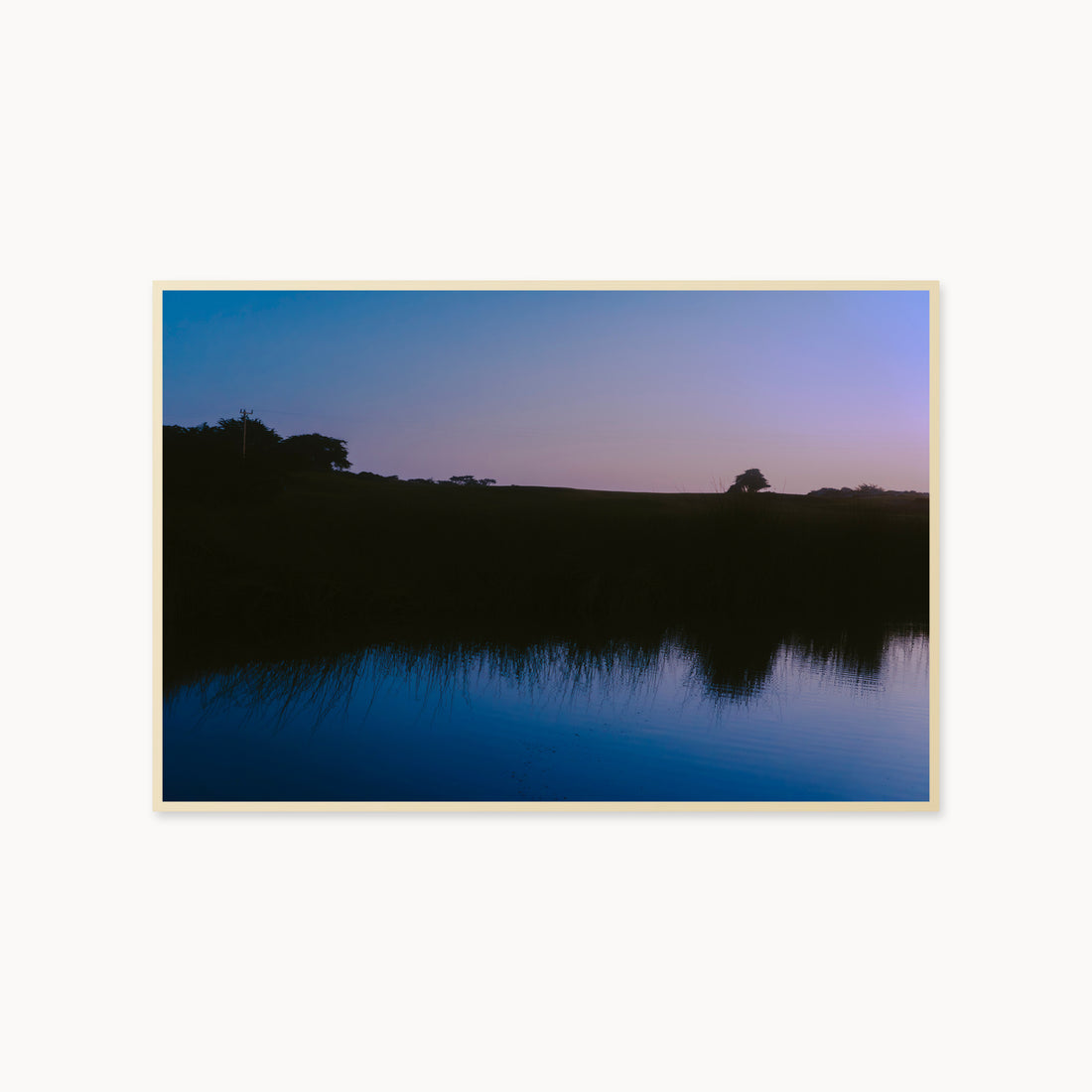 
What Lays Beneath — 40x60, maple frame. Dark trees and a twilight shoreline reflected across blue water.