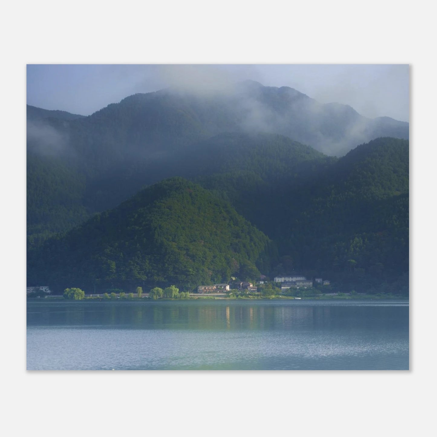 This misty lake mountain landscape wall art print captures serene blue tones and tranquil natural scenery, making it ideal for minimalist home decor. Designed for calming interiors, this fine art nature photography print enhances spaces with peaceful lake reflections, foggy mountain layers, and soft atmospheric light. A perfect choice for those seeking calming wall art, nature-inspired decor, or serene landscape prints for modern homes.