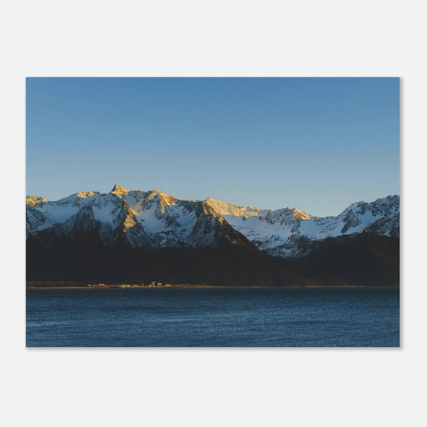 Snow-capped mountains reflecting in a body of water under a clear blue sky.