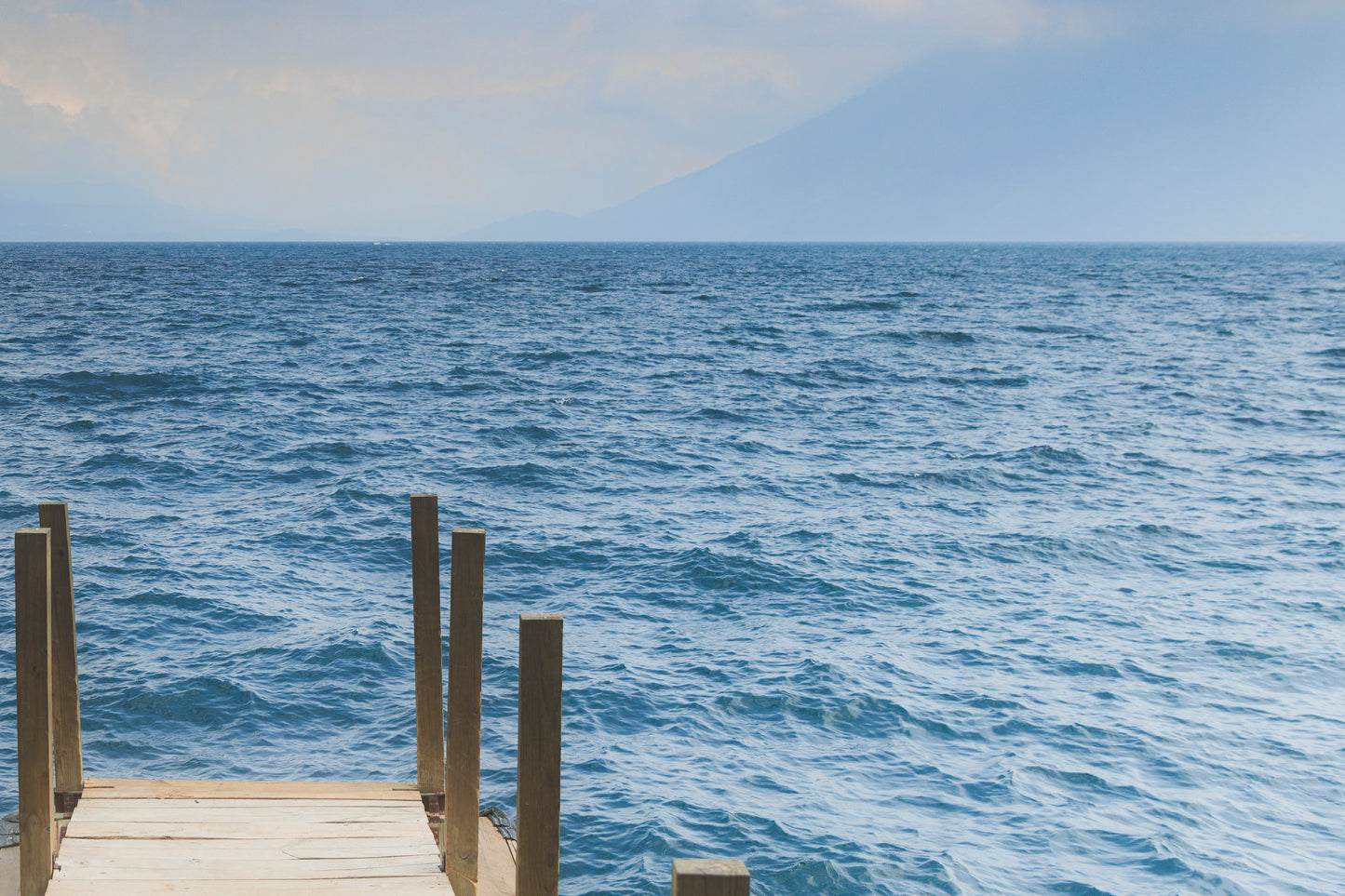 Wooden dock extending into a large body of water with a mountain in the background.