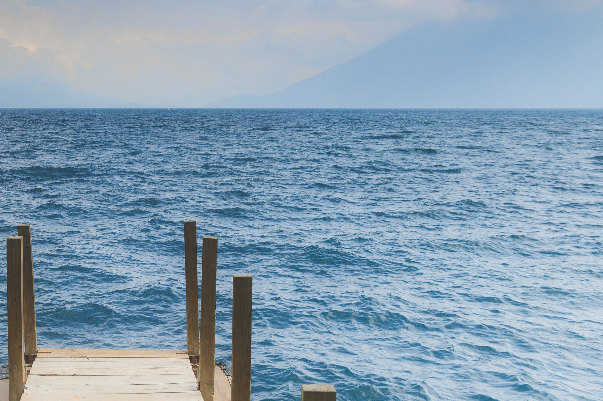 Wooden dock extending into a large body of water with a mountain in the background.